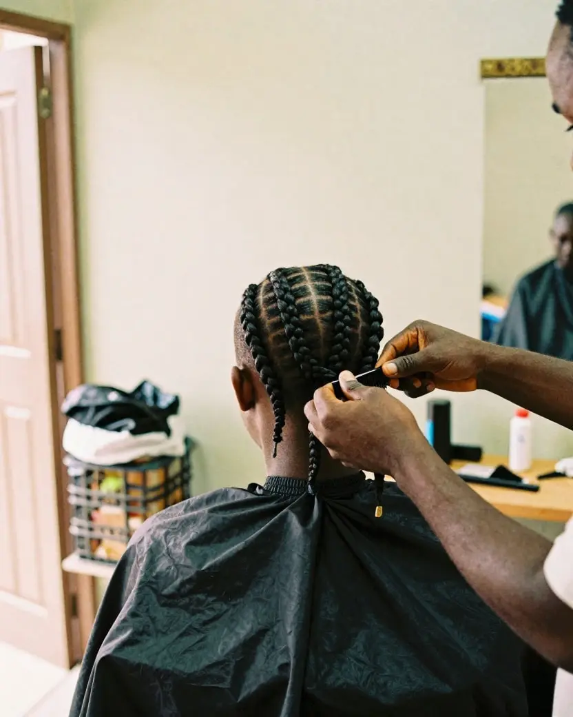 A hairdresser braiding cornrows in a neighbourhood salon