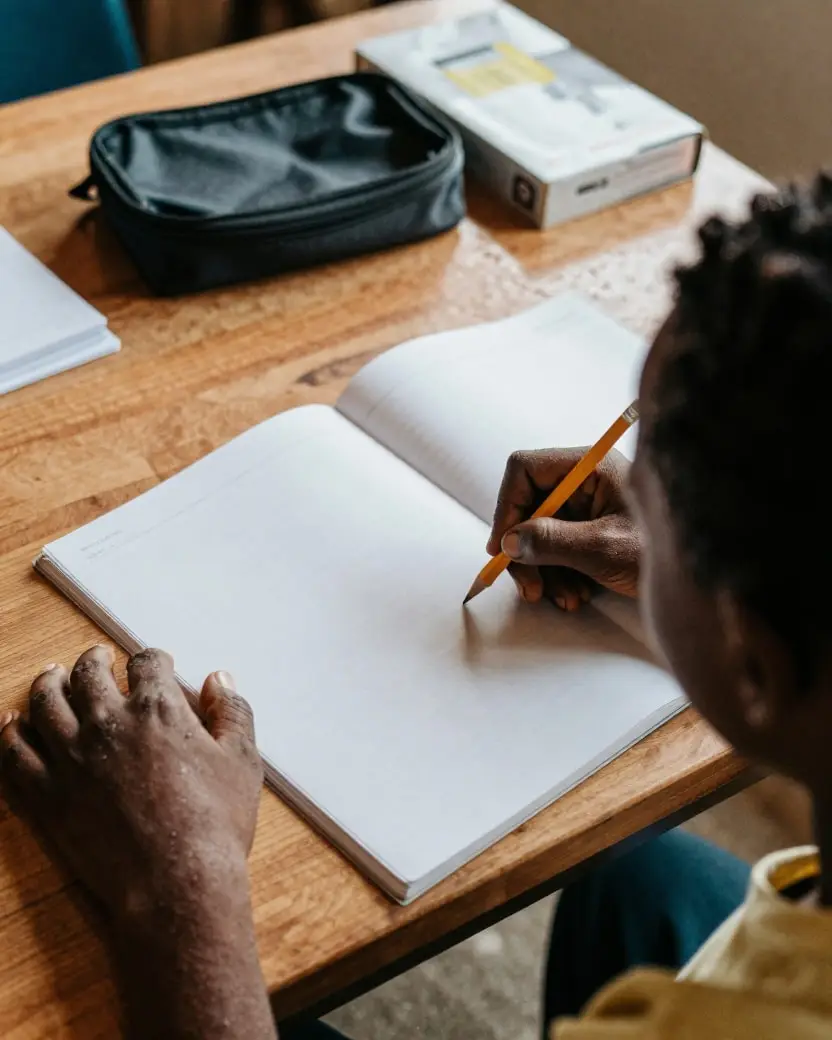 A child writing in an exercise book with an adult sitting beside them
