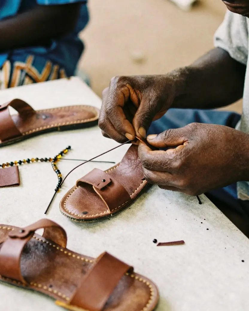 An artisan stitching a leather sandal at a workbench