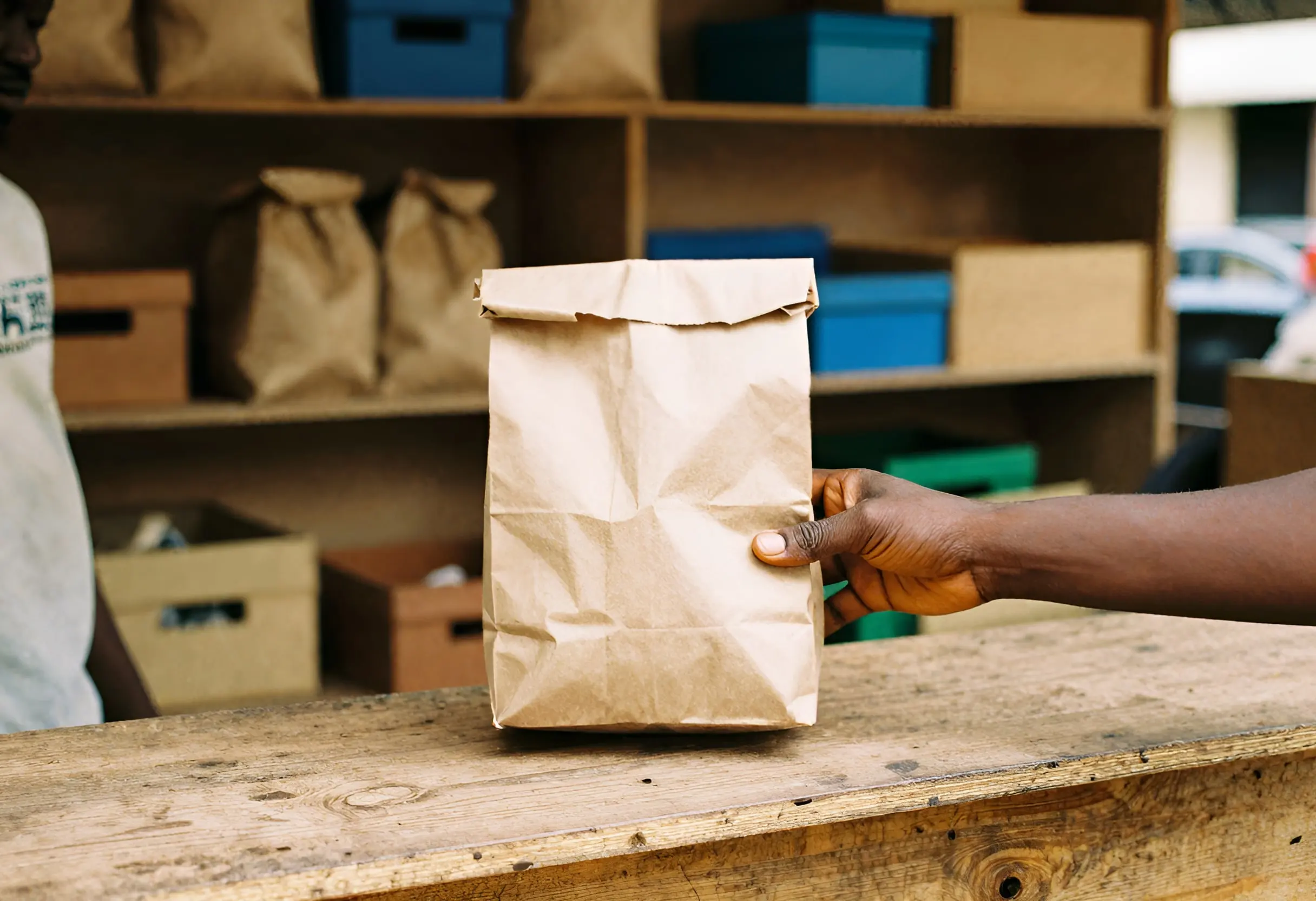 A hand taking a paper bag of goods from a wooden shop counter